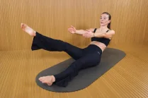 Flat Belly Flow session with Carlotta Gagna leaning back on a mat with one leg raised, the other bent, and arms reaching forward in Pilates Linfodrenante® Express